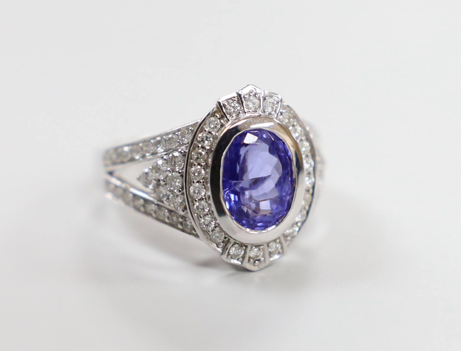 A modern 14k white metal, oval cut tanzanite and diamond chip set cluster dress ring, with diamond chip set shoulders, size M, gross weight 7 grams.